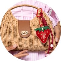 Woven straw handbag with a gold-colored clasp and a red-and-green strawberry bag charm – bag charm by SASSYCLASSY