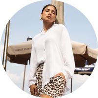 A woman wears an oversized beige muslin blouse with a button-down front, paired with leopard-print shorts – beige muslin blouses by SASSYCLASSY